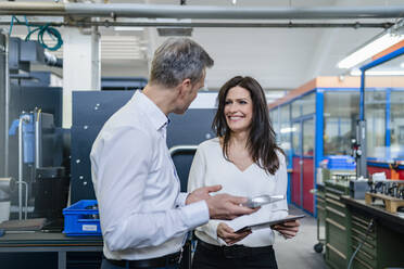 Businessman and businesswoman with product and tablet having a work meeting in a factory - DIGF10181