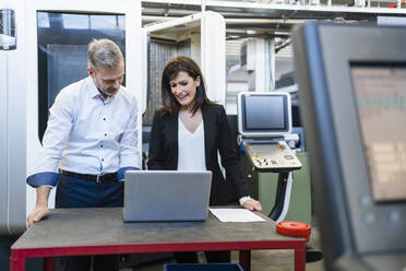 Businessman and businesswoman with laptop having a work meeting in a factory - DIGF10190