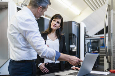 Businessman and businesswoman with laptop having a work meeting in a factory - DIGF10192