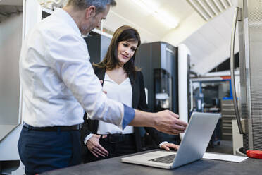 Businessman and businesswoman with laptop having a work meeting in a factory - DIGF10193