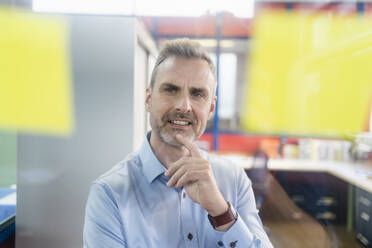 Portrait of a confident businessman looking at adhesive notes in a factory office - DIGF10226