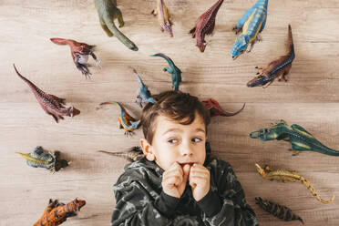 Porträt eines ängstlichen kleinen Jungen, der zwischen Spielzeugdinosauriern auf dem Boden liegt - JRFF04403