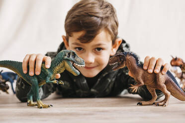 Lächelnder kleiner Junge liegt auf dem Boden und spielt mit Spielzeugdinosauriern - JRFF04405