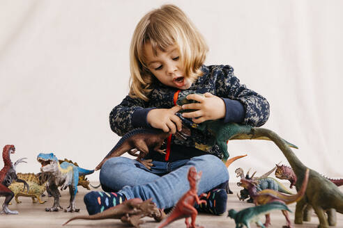 Porträt eines kleinen Mädchens, das auf dem Boden sitzt und mit Spielzeugdinosauriern spielt - JRFF04409