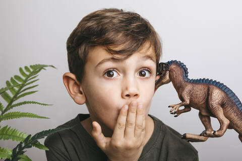 Porträt eines kleinen Jungen mit Spielzeugdinosaurier, der ein lustiges Gesicht zieht, lizenzfreies Stockfoto