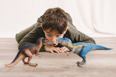 Porträt eines kleinen Jungen, der auf dem Boden hockt und mit Spielzeugdinosauriern spielt - JRFF04418