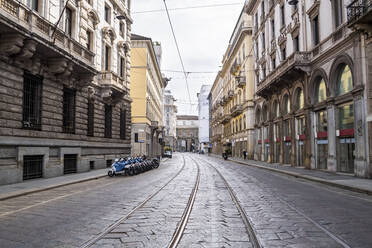 Italien, Mailand, Eisenbahnschienen, die sich während des COVID-19-Ausbruchs entlang einer leeren Straße erstrecken - MEUF00570