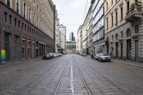 Italien, Mailand, Eisenbahnschienen, die sich während des COVID-19-Ausbruchs entlang einer leeren Straße erstrecken - MEUF00579