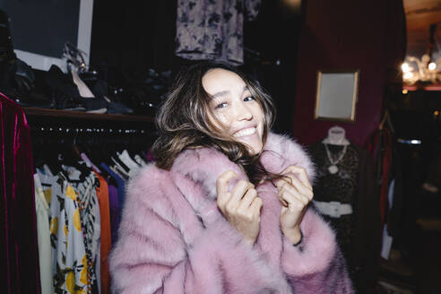 Portrait of smiling woman wearing pink fur jacket at thrift store - KNSF08003