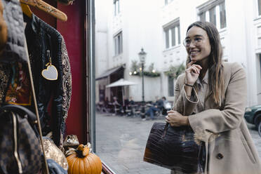 Smiling mid adult woman looking at window display of store in city - KNSF08006