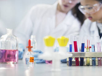 Studentinnen bei der Durchführung wissenschaftlicher Experimente hinter Reagenzgläsern und Flaschen in einem Laborklassenzimmer - CAIF26528