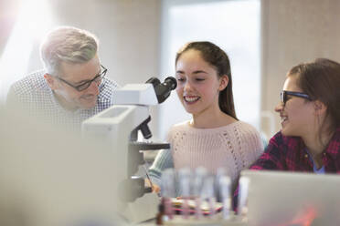 Ein männlicher Lehrer und ein Mädchen führen ein wissenschaftliches Experiment am Mikroskop in einem Laborklassenzimmer durch - CAIF26529