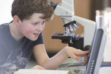 Junge Student, der ein wissenschaftliches Experiment am Mikroskop und am Computer in einem Laborklassenzimmer durchführt - CAIF26537