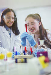 Smiling girl students examining liquid in test tube, conducting scientific experiment in laboratory classroom - CAIF26545