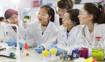 Curious students conducting scientific experiment, examining liquid in beaker in laboratory classroom - CAIF26558