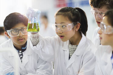 Curious students examining liquid in beaker, conducting scientific experiment in laboratory classroom - CAIF26567