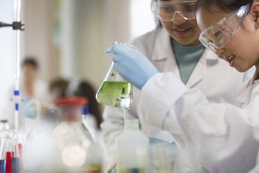 Girl students conducting scientific experiment, examining liquid in beaker in laboratory classroom - CAIF26584