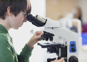Fokussierter Junge, der ein Mikroskop im Klassenzimmer benutzt - CAIF26619