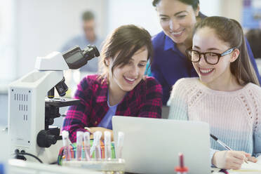 Lehrerin und Schülerin mit Mikroskop und Laptop, die ein wissenschaftliches Experiment im Labor durchführen - CAIF26625