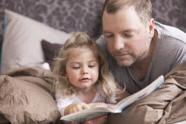 Vater und Tochter lesen ein Buch im Bett - SDAHF00782