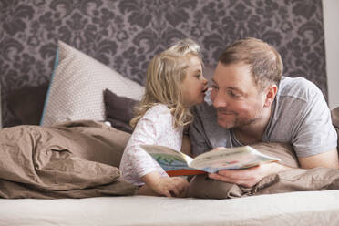 Father and daughter reading a book in bed, whispering in ear - SDAHF00783