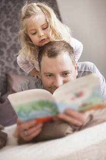 Father and daughter reading a book in bed - SDAHF00784