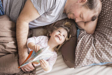 Father and daughter reading a book in bed - SDAHF00787