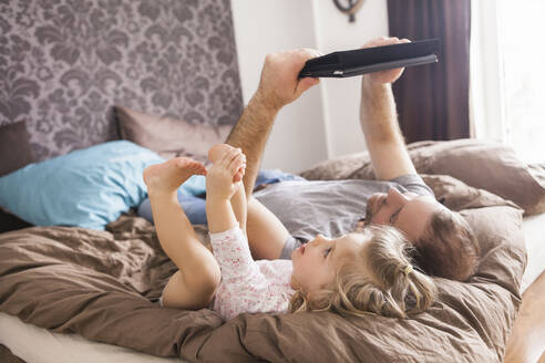 Vater und Tochter schauen auf ein Tablet, das im Bett liegt - SDAHF00788