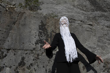 Frau mit gehäkeltem weißen Kopfschmuck mit Fransen vor einer Felswand - PSTF00690