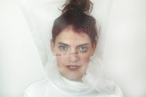 Portrait of redheaded young woman wearing transparent mask with question on it - PSTF00719
