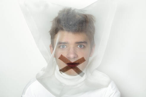 Portrait of teenage boy wearing transparent mask with cross on his mouth - PSTF00736