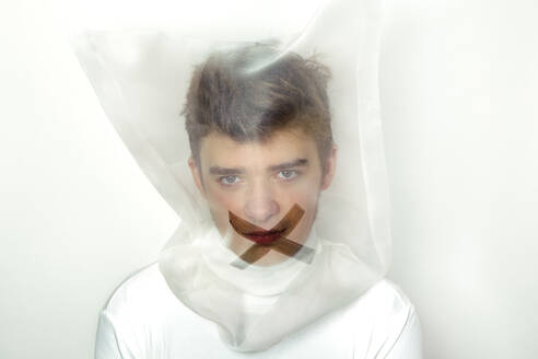 Portrait of teenage boy wearing transparent mask with cross on his mouth - PSTF00738