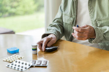 Mittelteil eines älteren Mannes mit Diabetes im Ruhestand, der sich selbst untersucht, während er am Tisch sitzt - AFVF06164