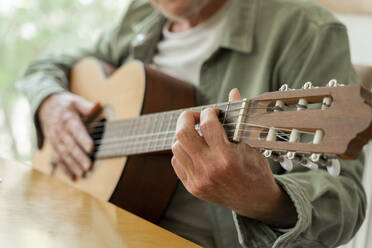 Mittelteil eines Mannes im Ruhestand, der zu Hause sitzend Gitarre übt - AFVF06175