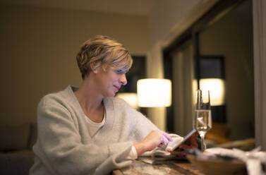 Blonde Frau, die noch spät arbeitet und ein digitales Tablet in einem beleuchteten Wohnzimmer benutzt - BFRF02242
