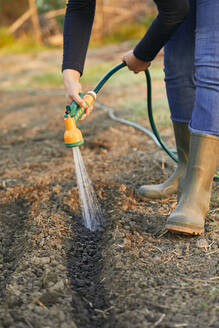 Low section of woman watering with garden hose - ZEDF03360