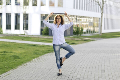 Porträt einer Geschäftsfrau mit Laptop, die auf einem Bein balanciert, lizenzfreies Stockfoto