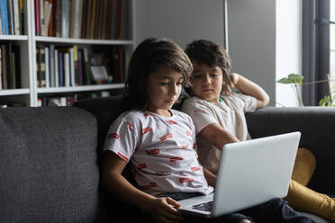 Geschwister sitzen mit Laptop auf dem Sofa im heimischen Wohnzimmer - VABF02896