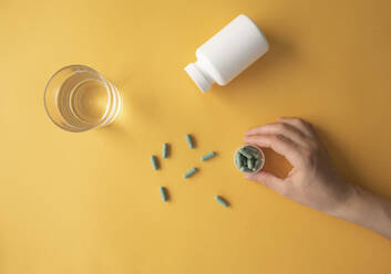 Studio shot of glass of water and hand of woman taking nutritional supplement capsules - MOMF00852