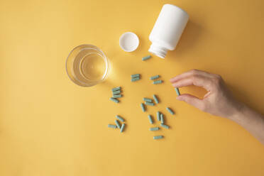Studio shot of glass of water and hand of woman taking nutritional supplement capsules - MOMF00854