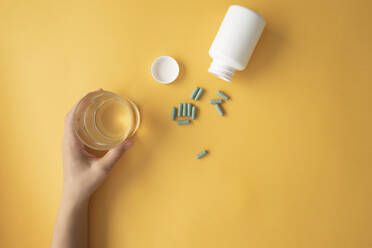 Studio shot of nutritional supplement capsules and hand of woman picking up glass of water - MOMF00855