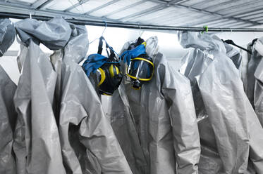 Protective suits and masks hanging from rack in locker room - JCMF00654