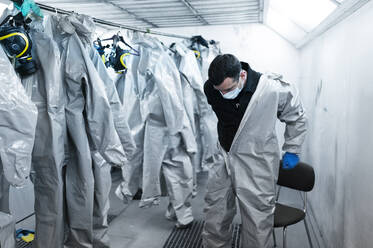 Healthcare worker wearing protective suit in locker room - JCMF00656