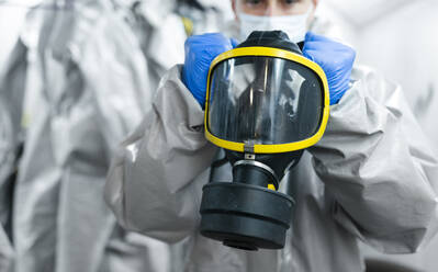 Close-up of sanitation worker holding gas mask while getting dressed in locker room - JCMF00657