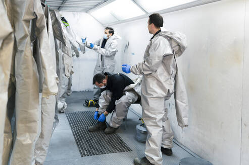 Sanitärarbeiter, die sich in der Umkleidekabine Schutzanzüge anziehen - JCMF00660