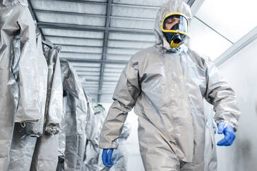 Low angle view of disinfection worker in protective suit walking inside locker room during COVID-19 crisis - JCMF00662