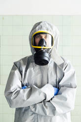 Portrait of sanitation worker in protective suit while standing with arms crossed against wall - JCMF00672