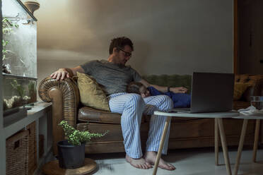 Mann sitzt bei seiner kranken Tochter, die während der Quarantäne zu Hause auf dem Sofa im Wohnzimmer schläft - ERRF03636