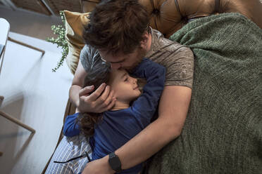 High angle view of father hugging her sick daughter to sleep on sofa in living room - ERRF03651