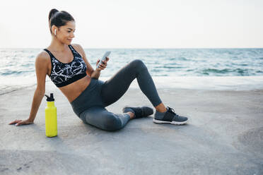 Lächelnde junge Frau, die nach dem Sport auf der Promenade ihr Smartphone benutzt - OYF00131